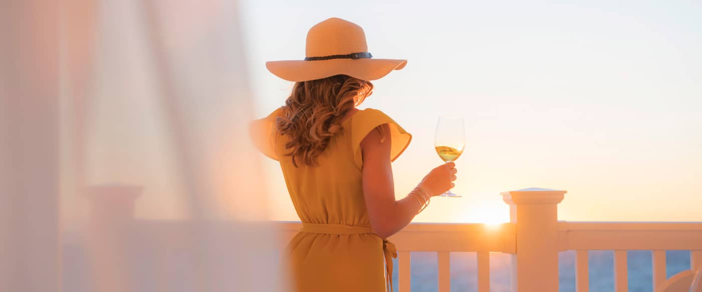 Woman on lakefront balcony with wine, golden hour, Inn at Bay Harbor
