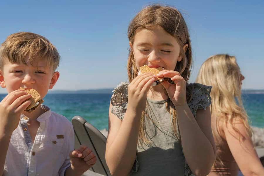 Young brother and sister eat s'mores along water, Inn at Bay Harbor